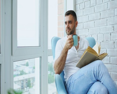 Person resting on a comfortable chair with a book in a cozy apartment
